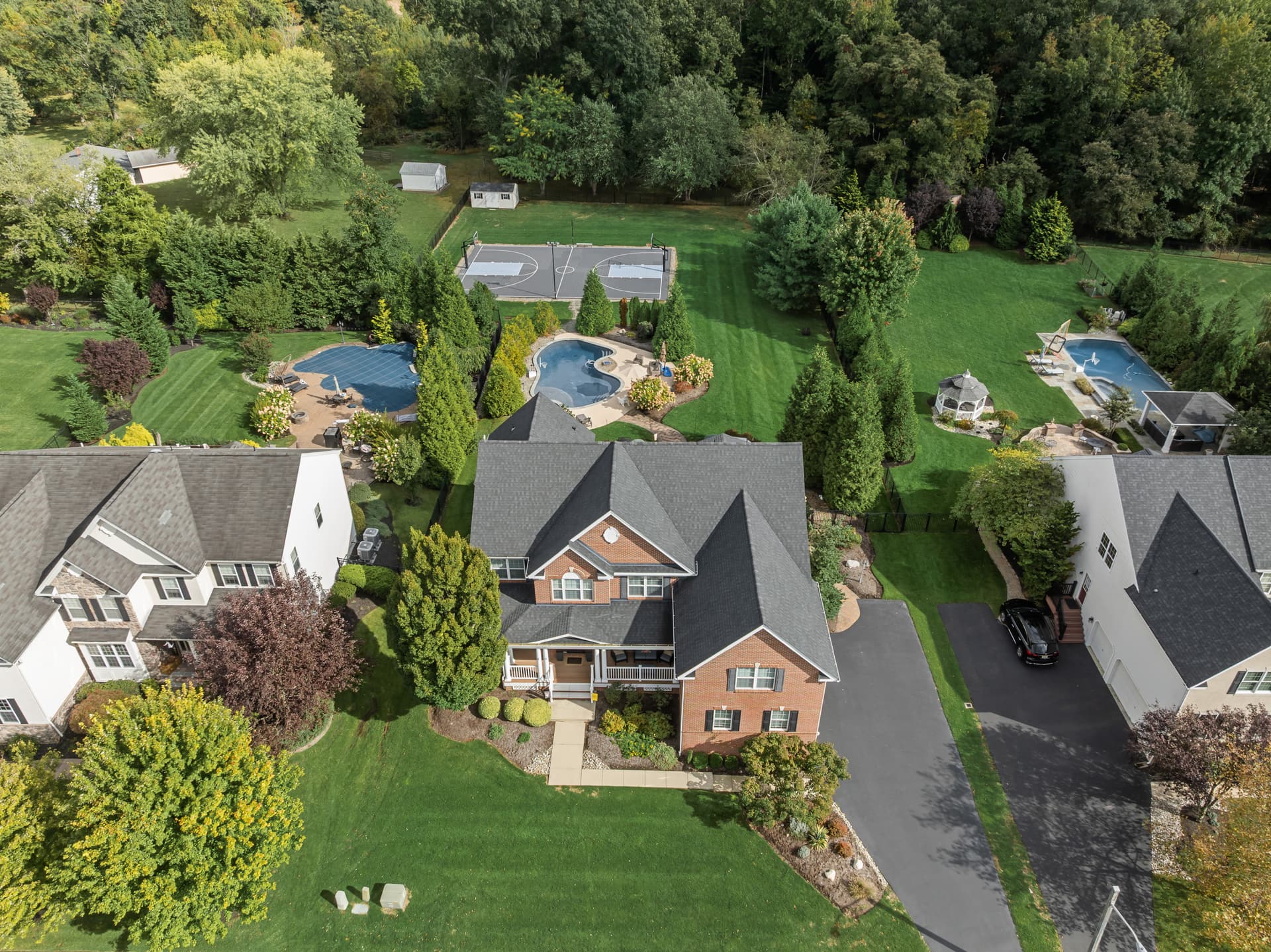 Drone photo of a backyard with a pool and sport court behind a brick home, Mount Laurel, NJ
